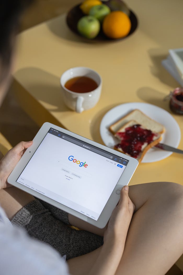 services-05 Person using a tablet with Google search open while having breakfast with toast and tea.